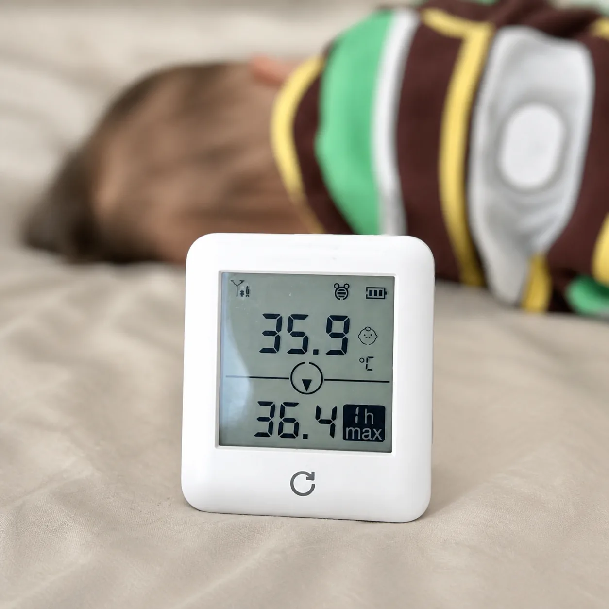 P20 bedside temperature monitor standing on a bed beside a sleeping baby, its screen showing 35.9 °C