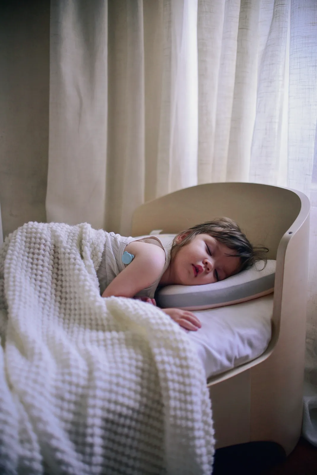 Child asleep in a crib wearing the P20 fever monitor