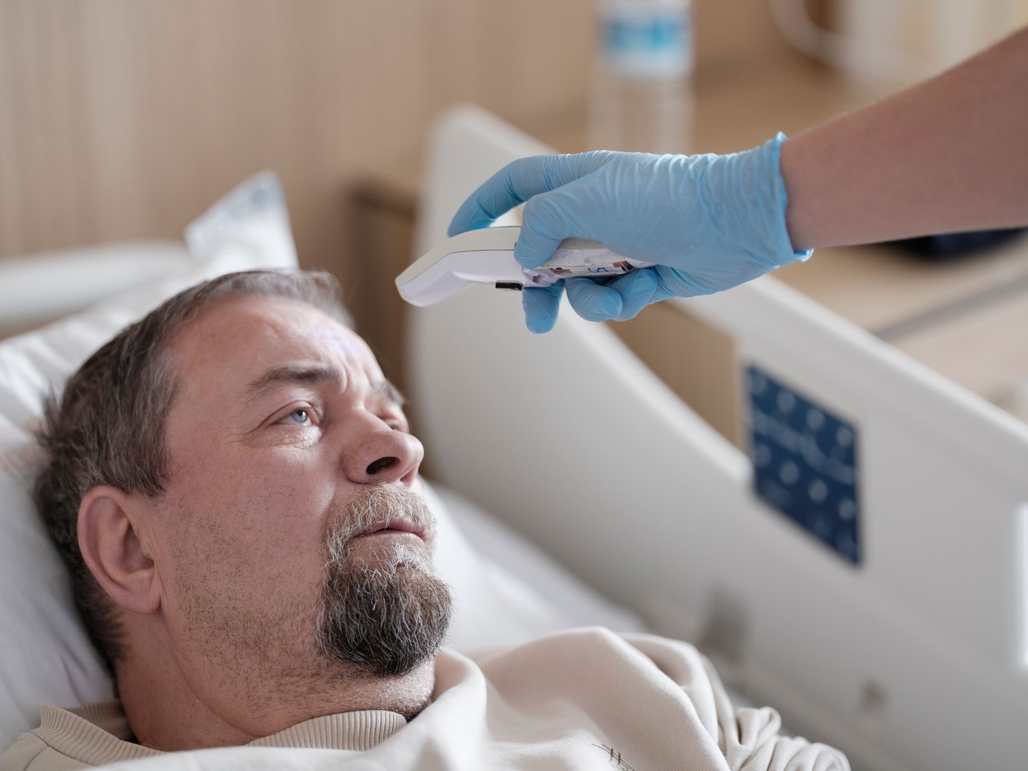 A nurse checks a patient's temperature at the bedside with a handheld thermometer